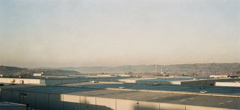 Wide industrial landscape with warehouse roofs and hills at dawn