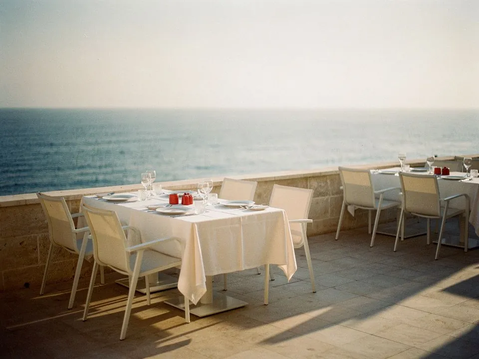 Sunny hotel terrace with set tables and empty chairs facing the sea