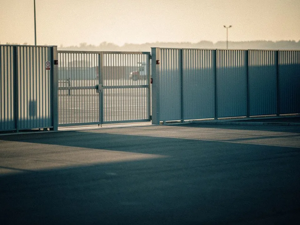 Secure logistics yard with a closed steel gate and tall fence at dawn