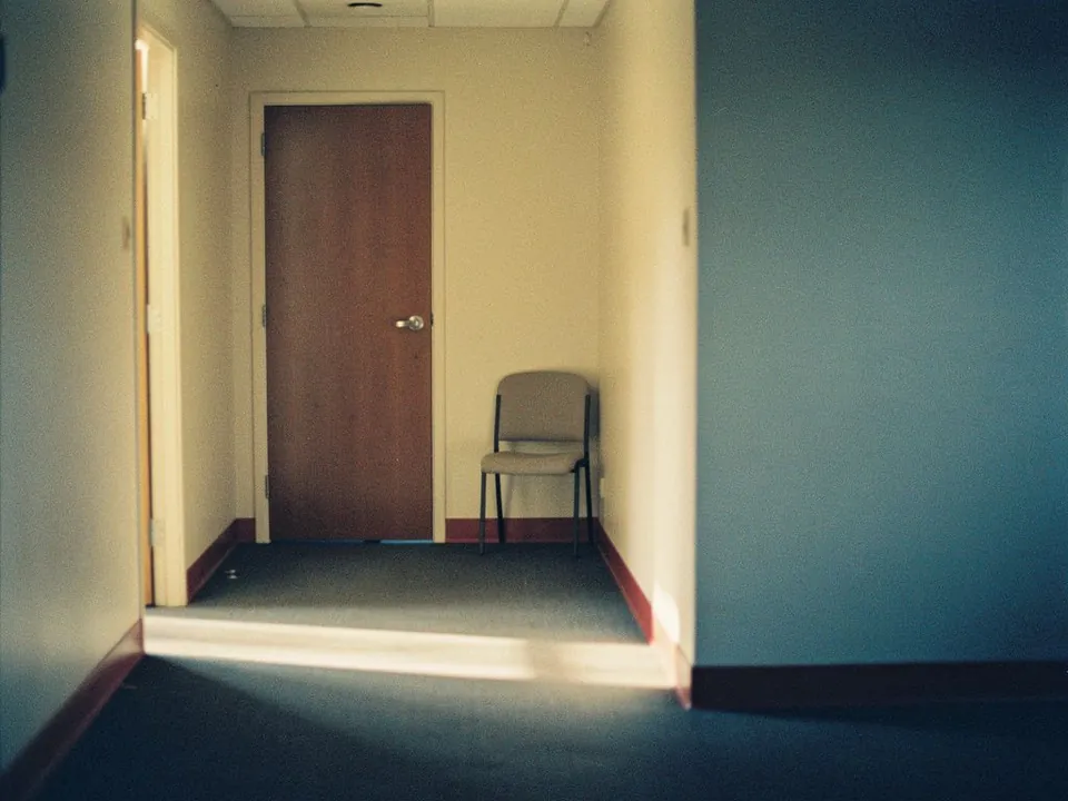 Closed wooden office door at the end of a quiet corridor with a chair